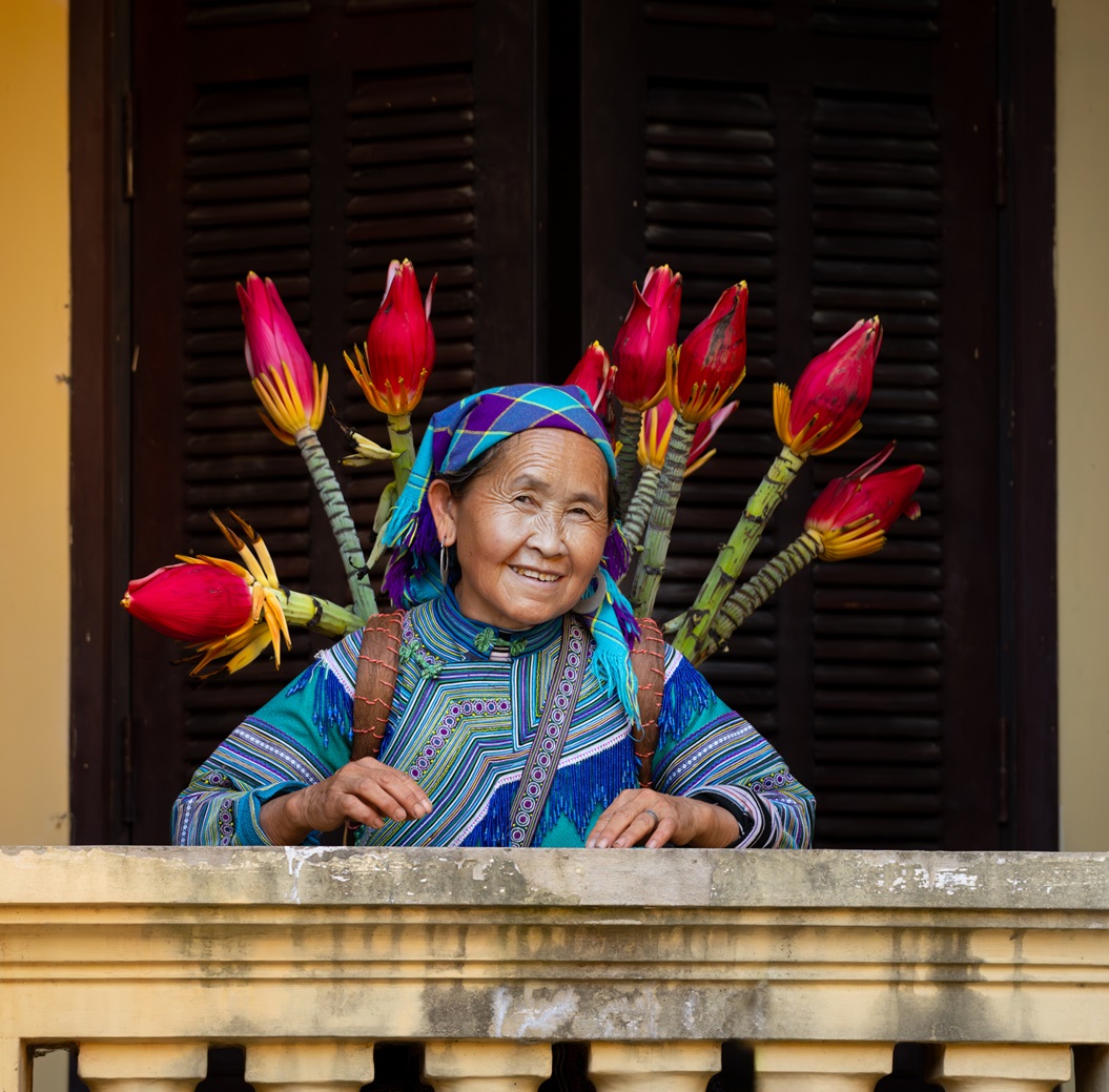Lächelnde Hmong-Frau mit einem Korb voller Blumen im Palast der Hmong-Könige (Vau Mean) in Bac Ha, Provinz Lao Cai, Vietnam